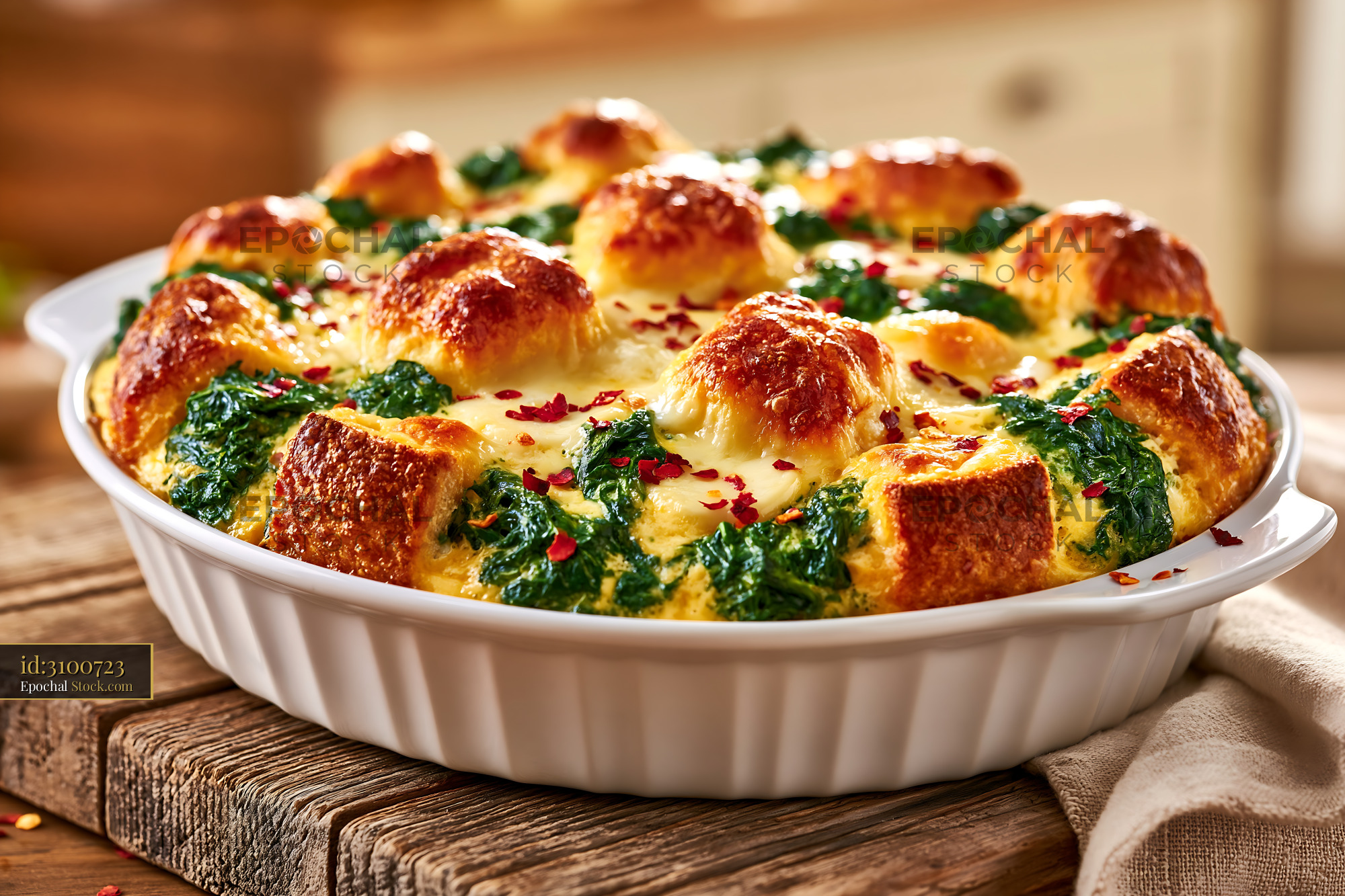 Baked egg strata with spinach and bread cubes on a wooden table - stock photo