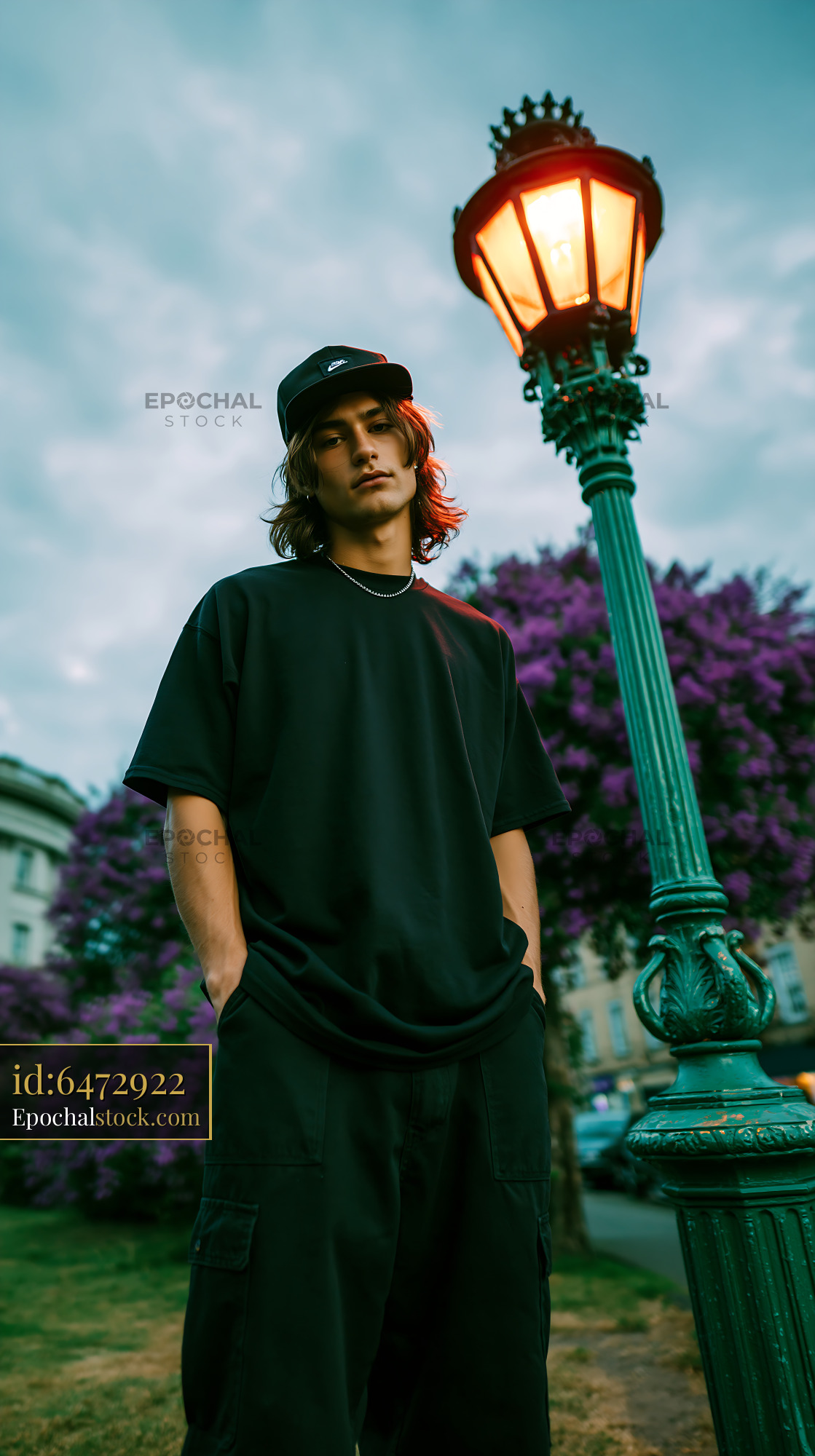 Watermarked full-resolution preview of Young man standing by a lamppost near purple flowers in a park