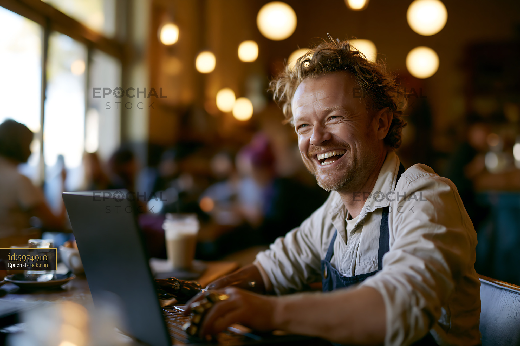 Watermarked full-resolution preview of Man smiles while working on laptop in a coffee shop