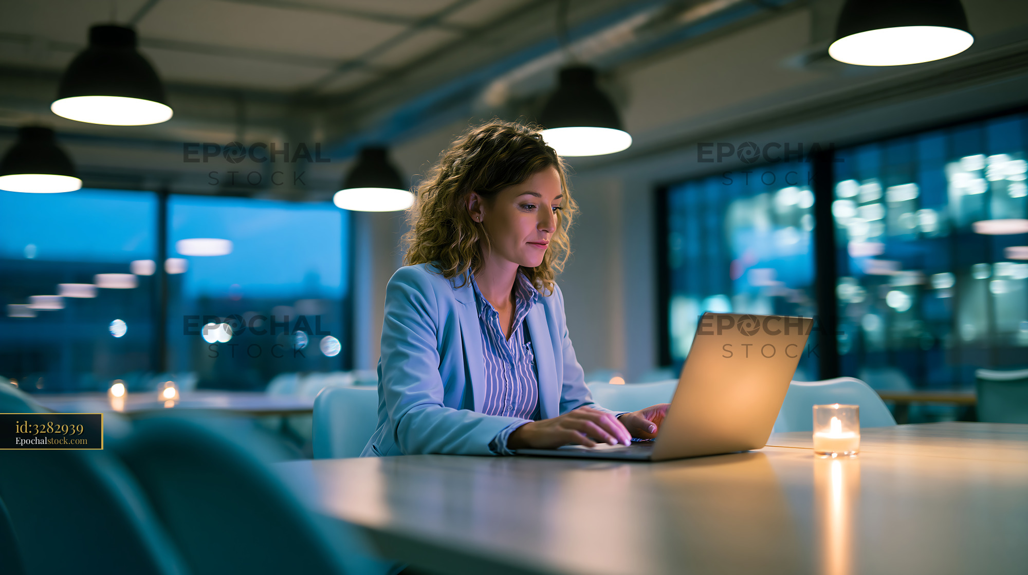 Watermarked full-resolution preview of Woman working on laptop in modern office at night