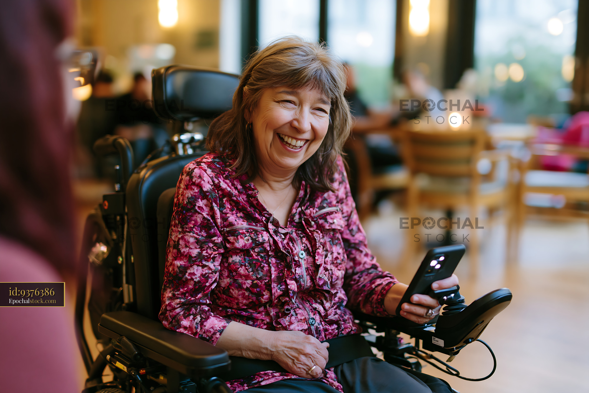 Watermarked full-resolution preview of Woman in wheelchair smiling while using smartphone indoors