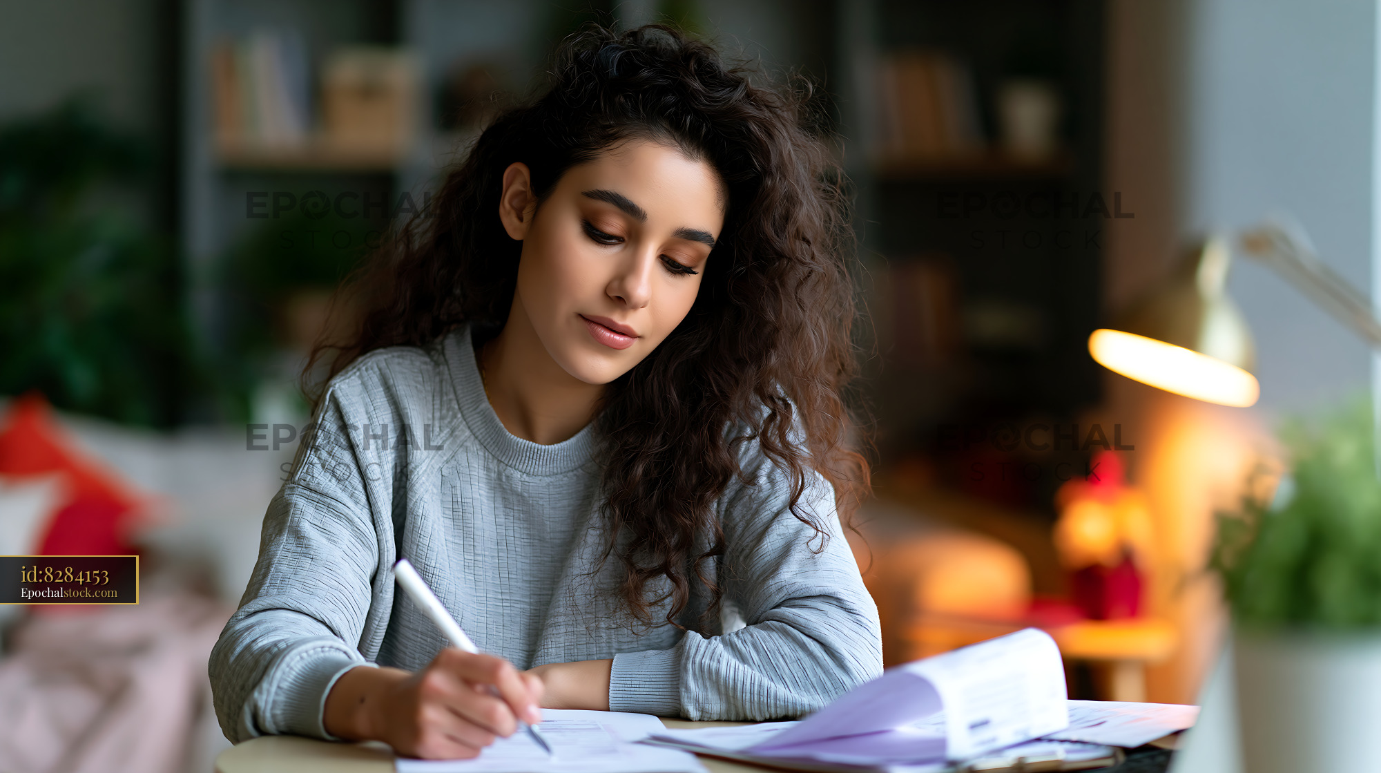 Watermarked full-resolution preview of Young woman writing in a notebook at home in the evening