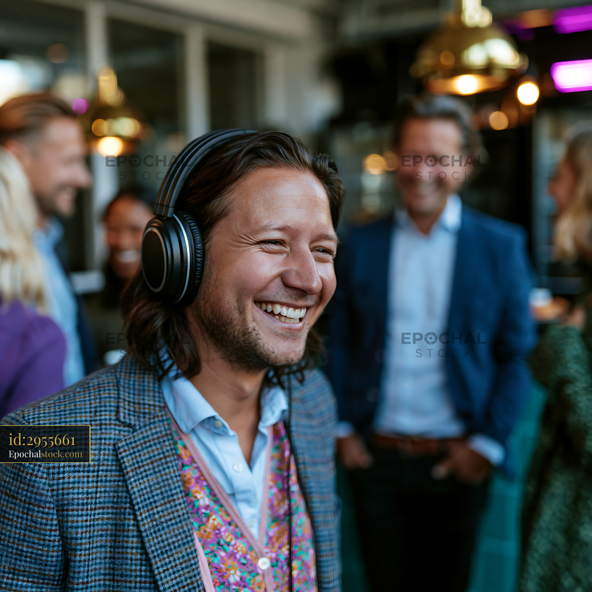 Watermarked full-resolution preview of Happy man with headphones in a warmly lit indoor gathering