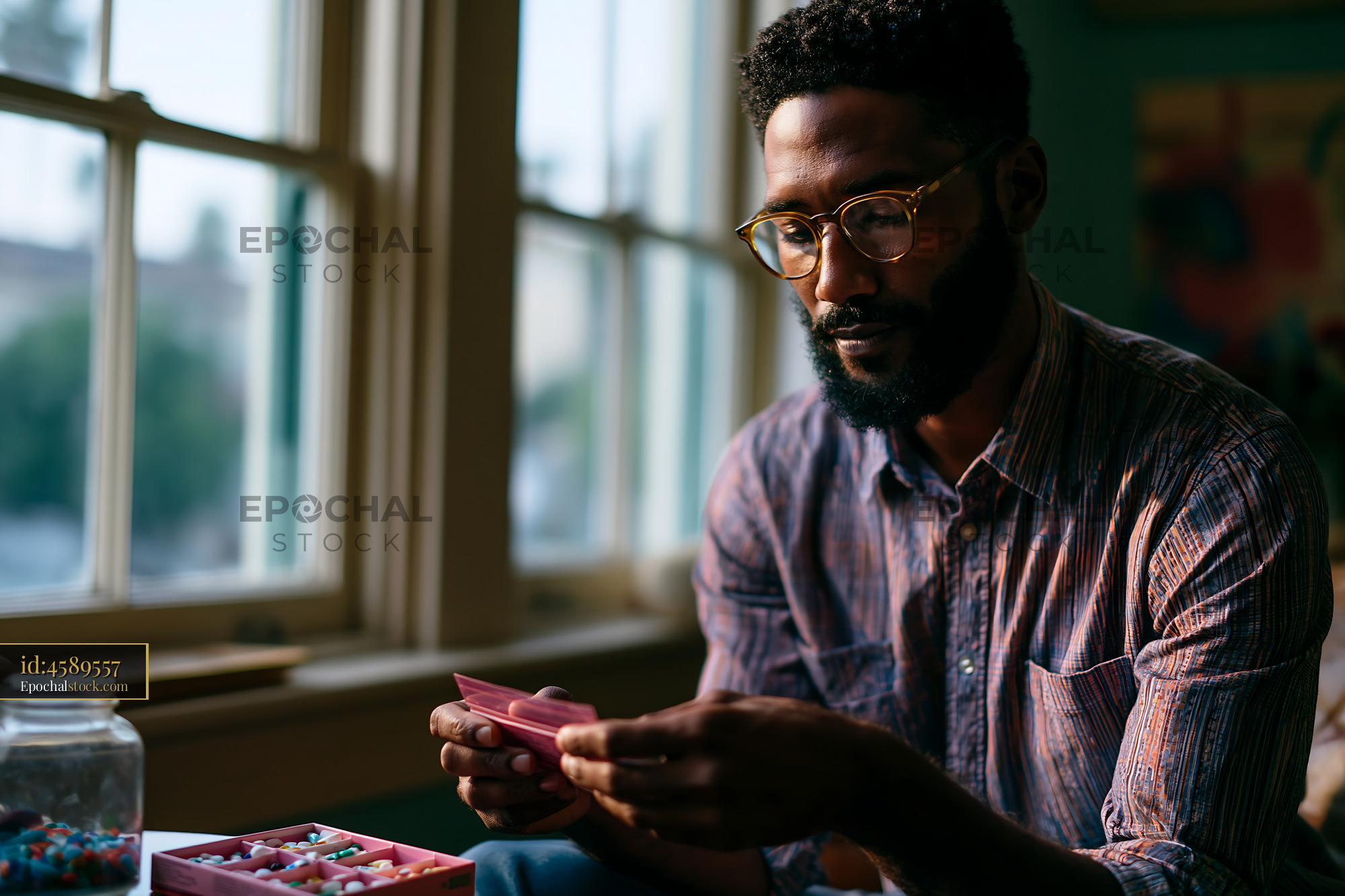 Watermarked full-resolution preview of Man sorting pills in a bright room with windows