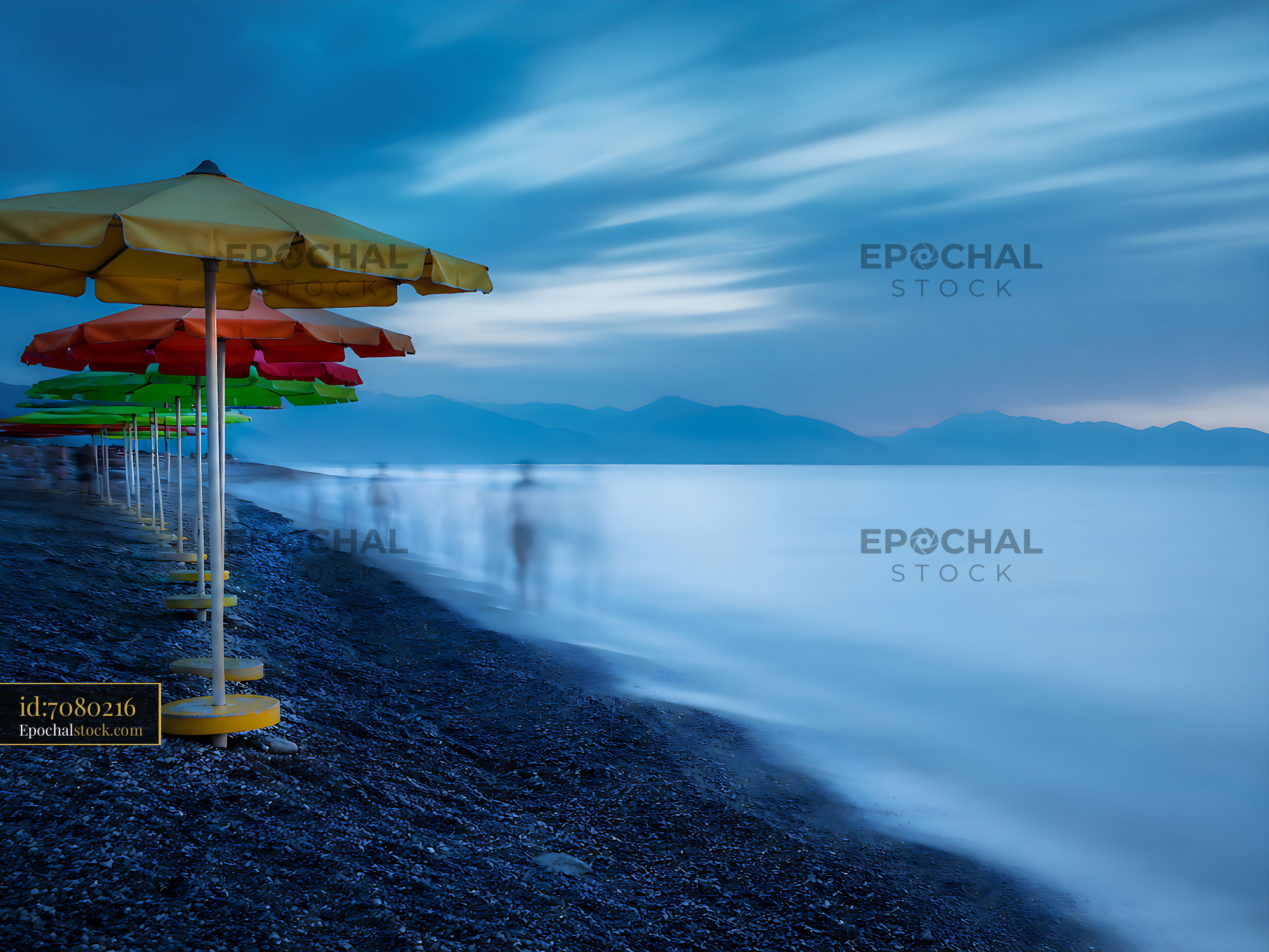 Watermarked full-resolution preview of Beach umbrellas by the sea at dusk with blurred figures