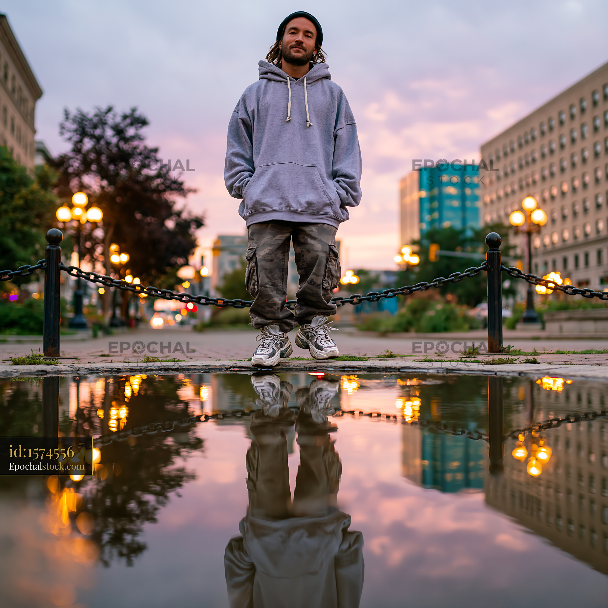 Confident Young Man Standing in Oversized Hoodie by Urban Reflection - stock photo