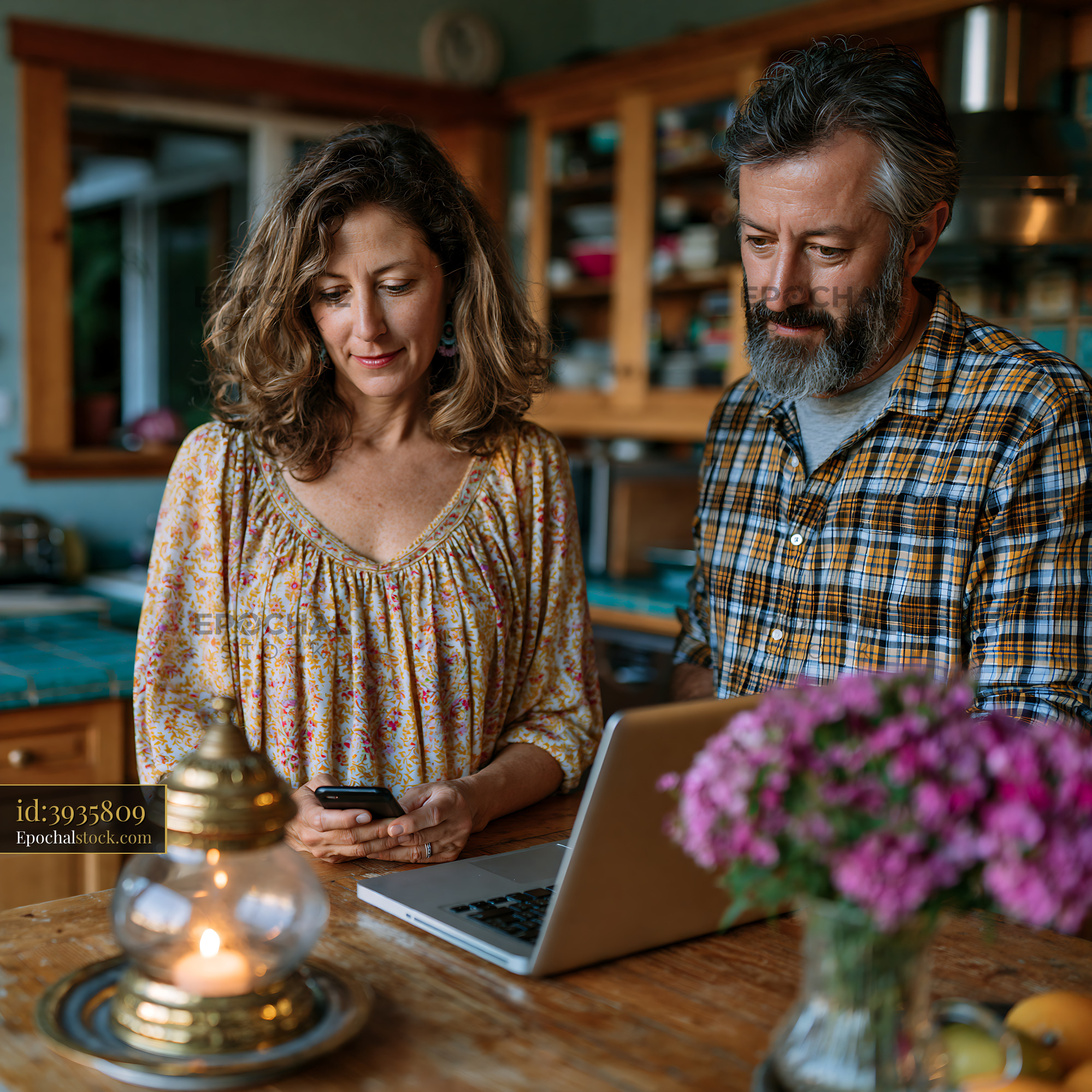 Watermarked full-resolution preview of Couple using a laptop and smartphone in a cozy kitchen
