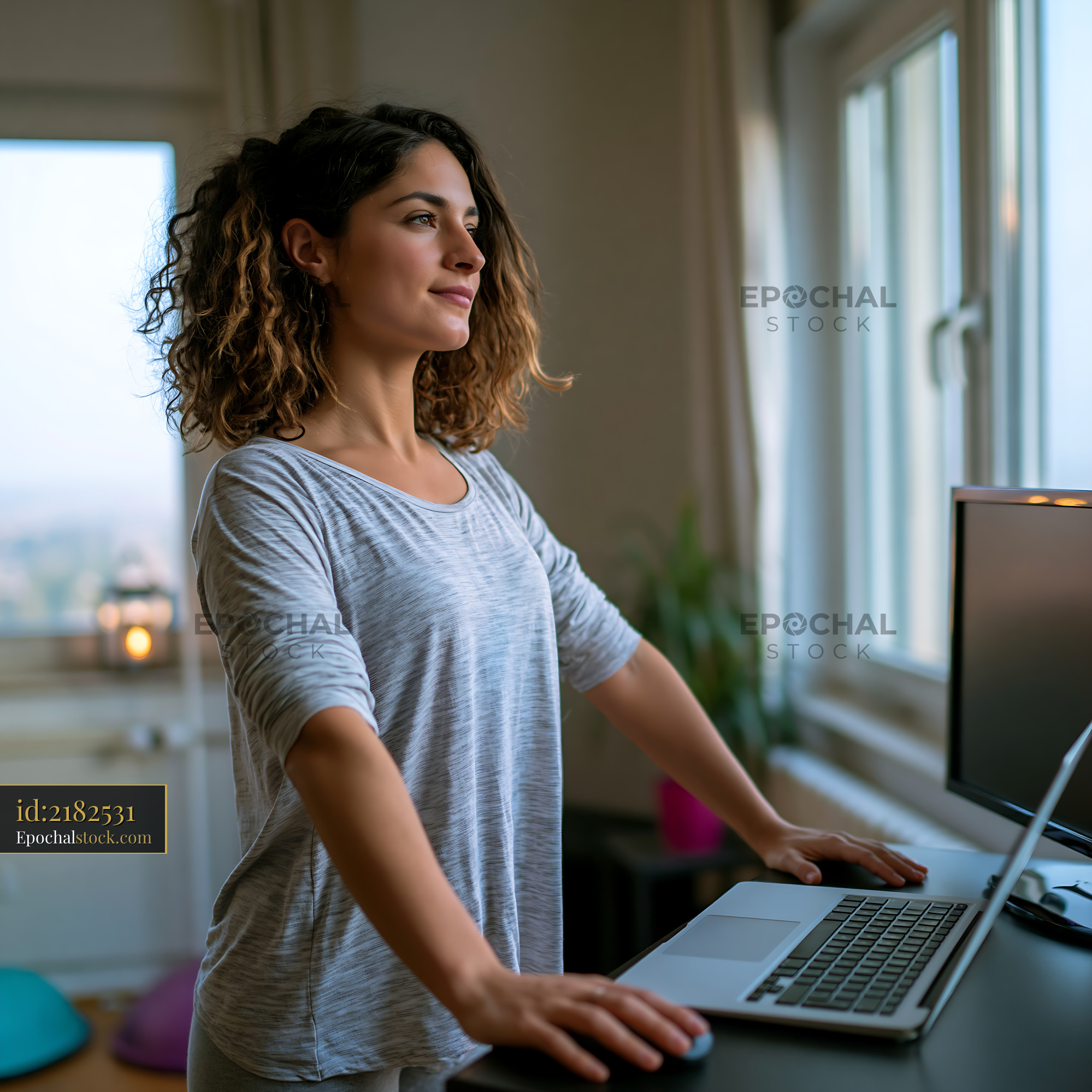 Watermarked full-resolution preview of Woman standing at desk while working on laptop in home office