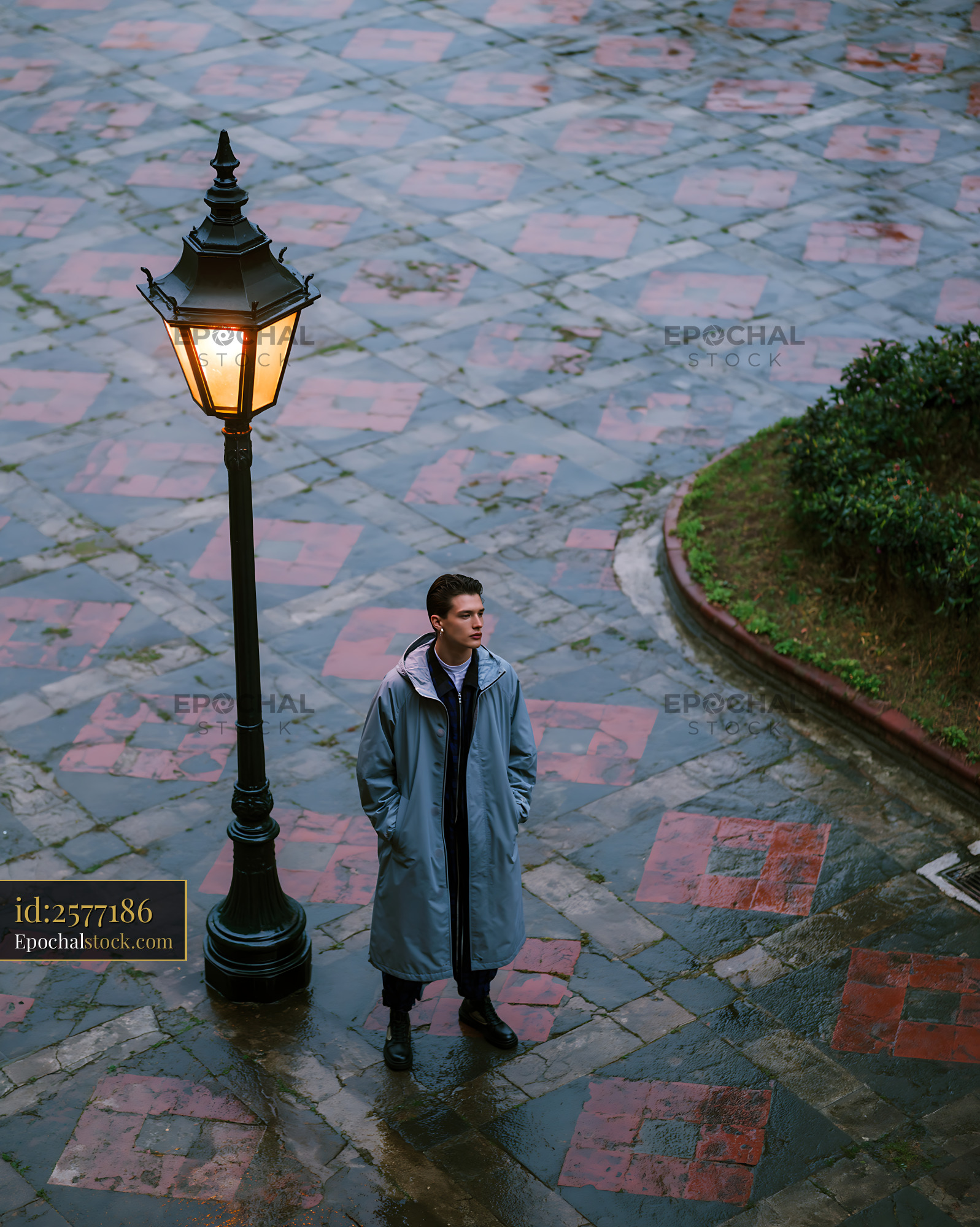 Watermarked full-resolution preview of Man standing by street lamp on wet pavement during rainy weather