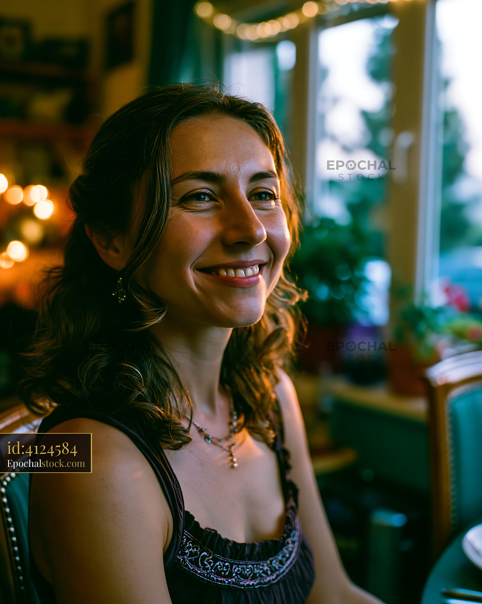 Watermarked full-resolution preview of Woman smiling by the window with warm lights in the background