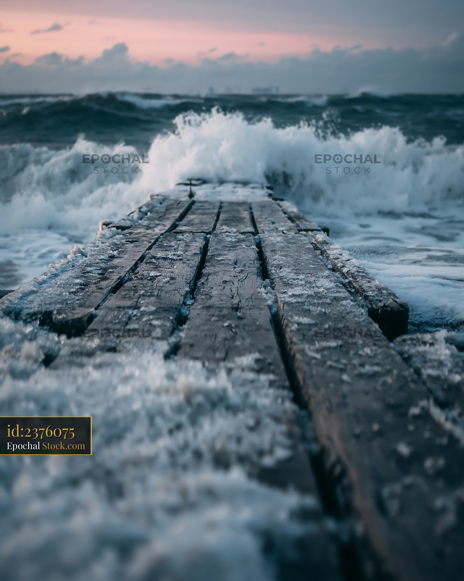 Frozen wooden pier facing crashing waves in a stormy sea at winter dus - stock photo