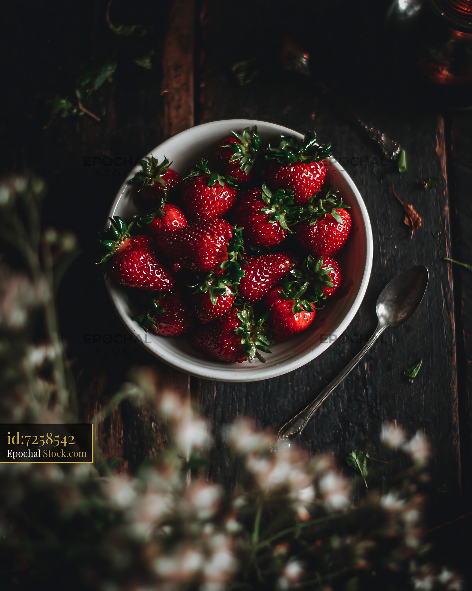 Fresh strawberries in a white bowl on a rustic wooden table at a garde - stock photo