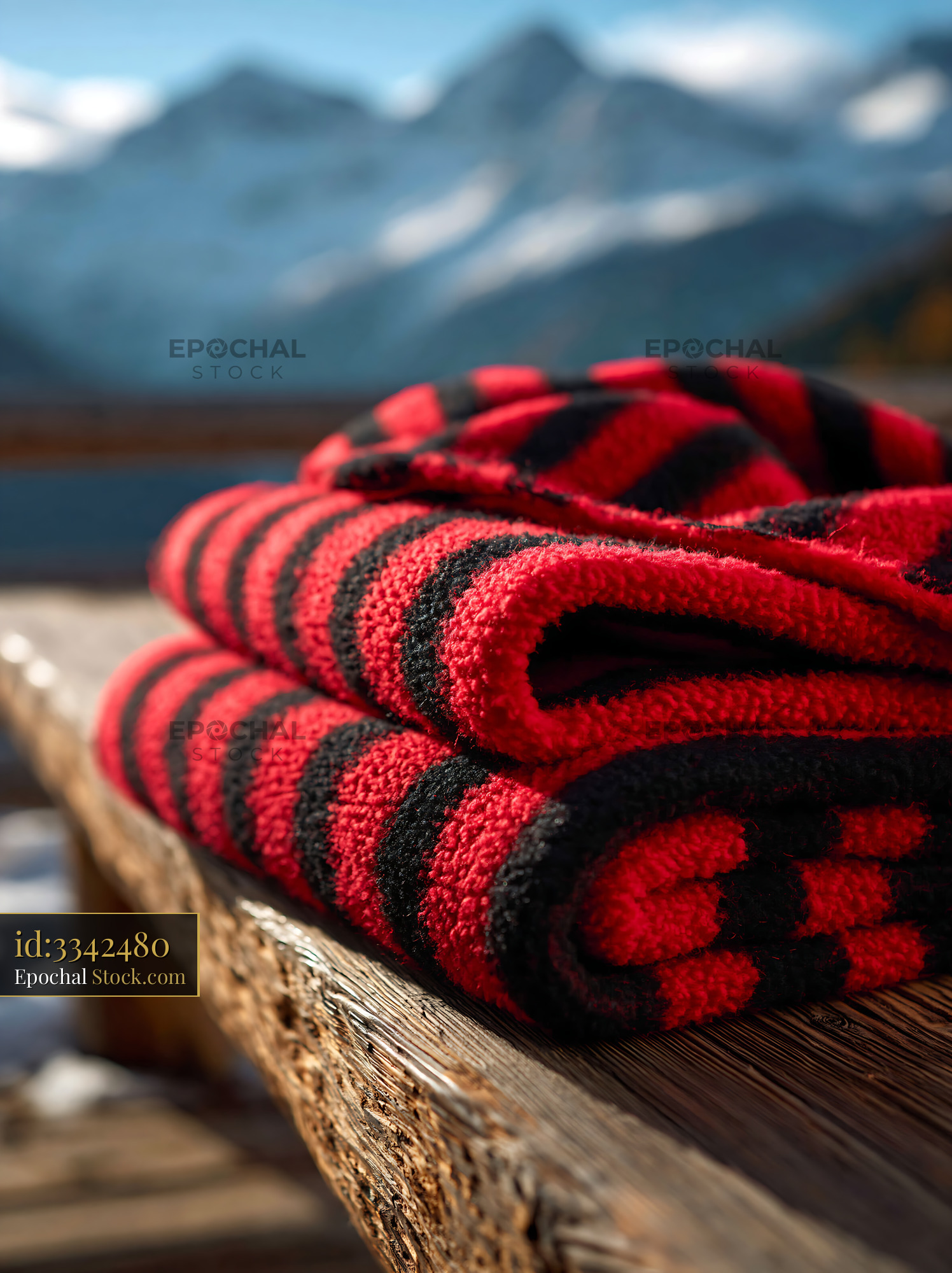 Red and black striped throw on bench against snowy mountain backdrop - stock photo