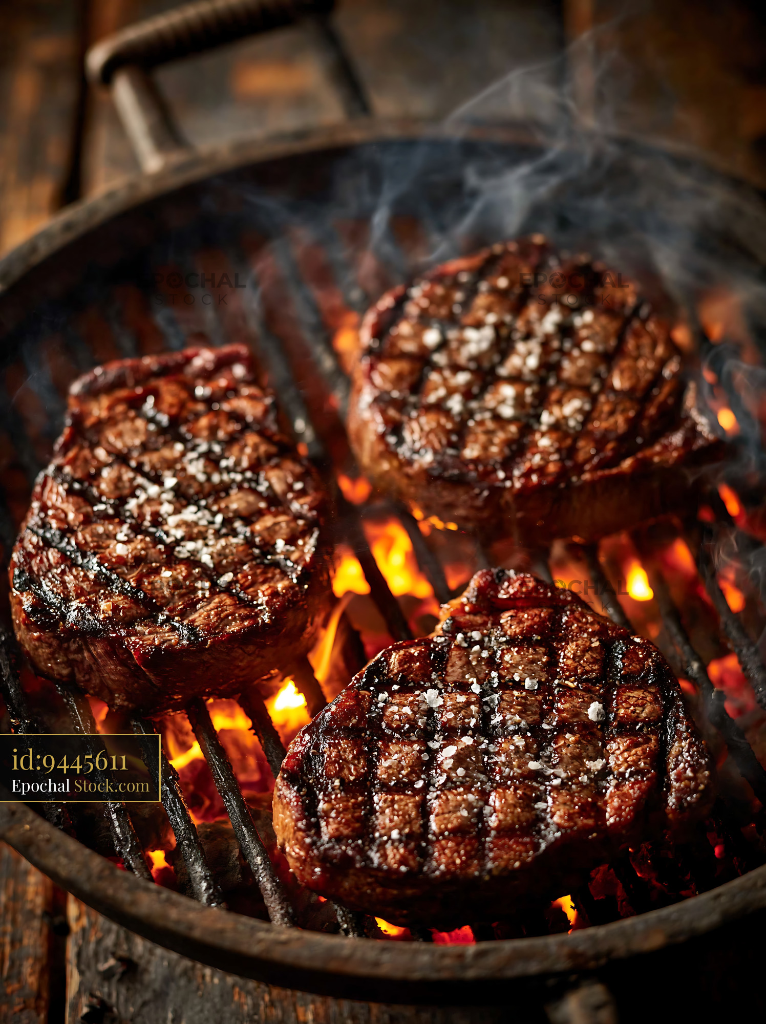 Three juicy beef steaks grilling over an open fire with smoke - stock photo