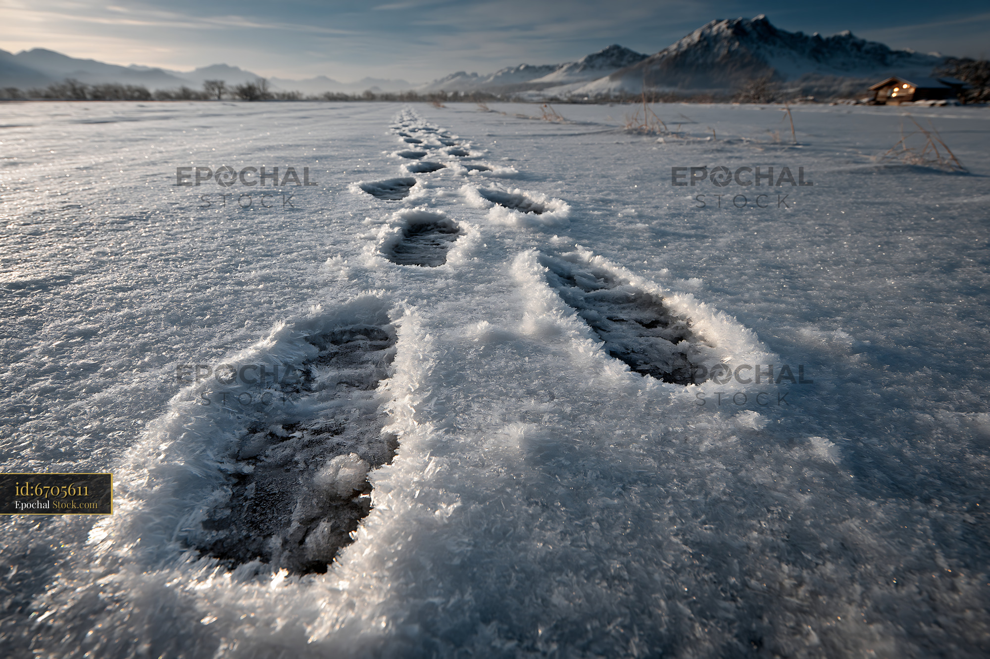 Footprints in deep snow leading toward a distant mountain cabin - stock photo