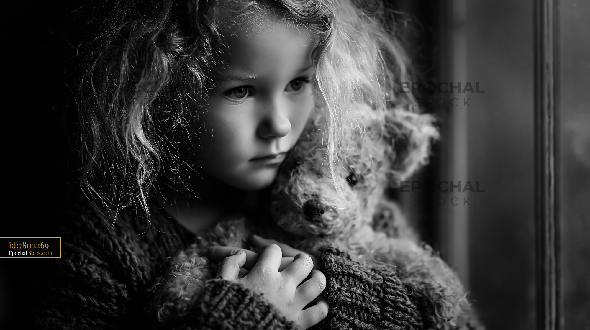 Little girl with curly hair clutching a teddy bear by a window - stock photo