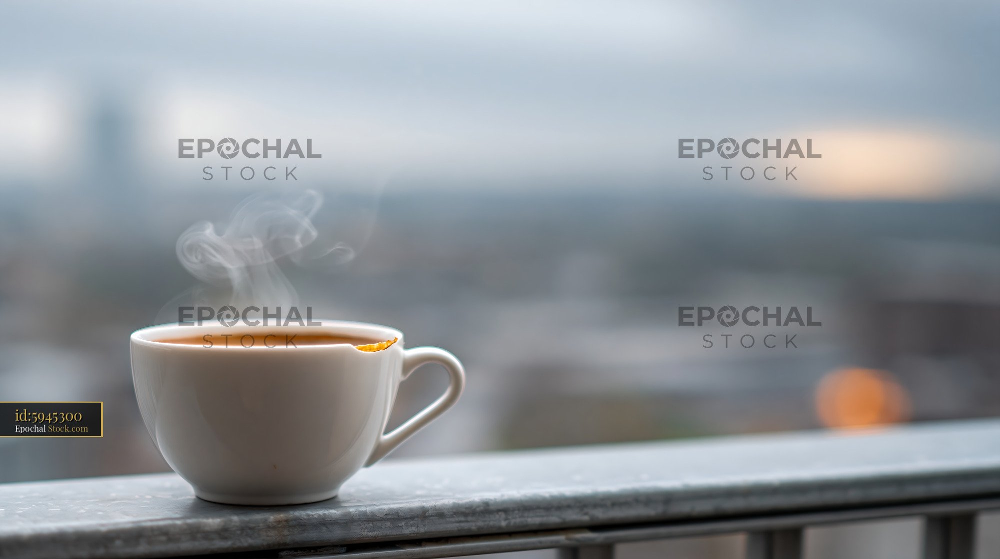 Steaming coffee cup on a city balcony at dawn - stock photo