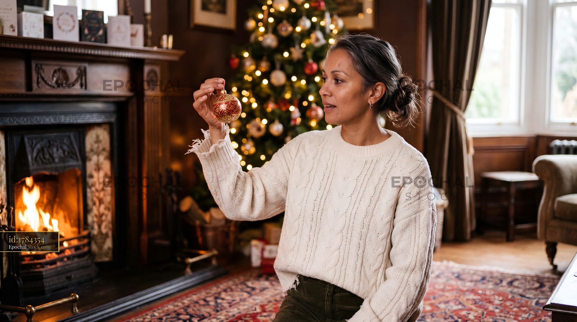 Woman holding ornament near Christmas tree and fireplace Premium Stock Image - stock photo