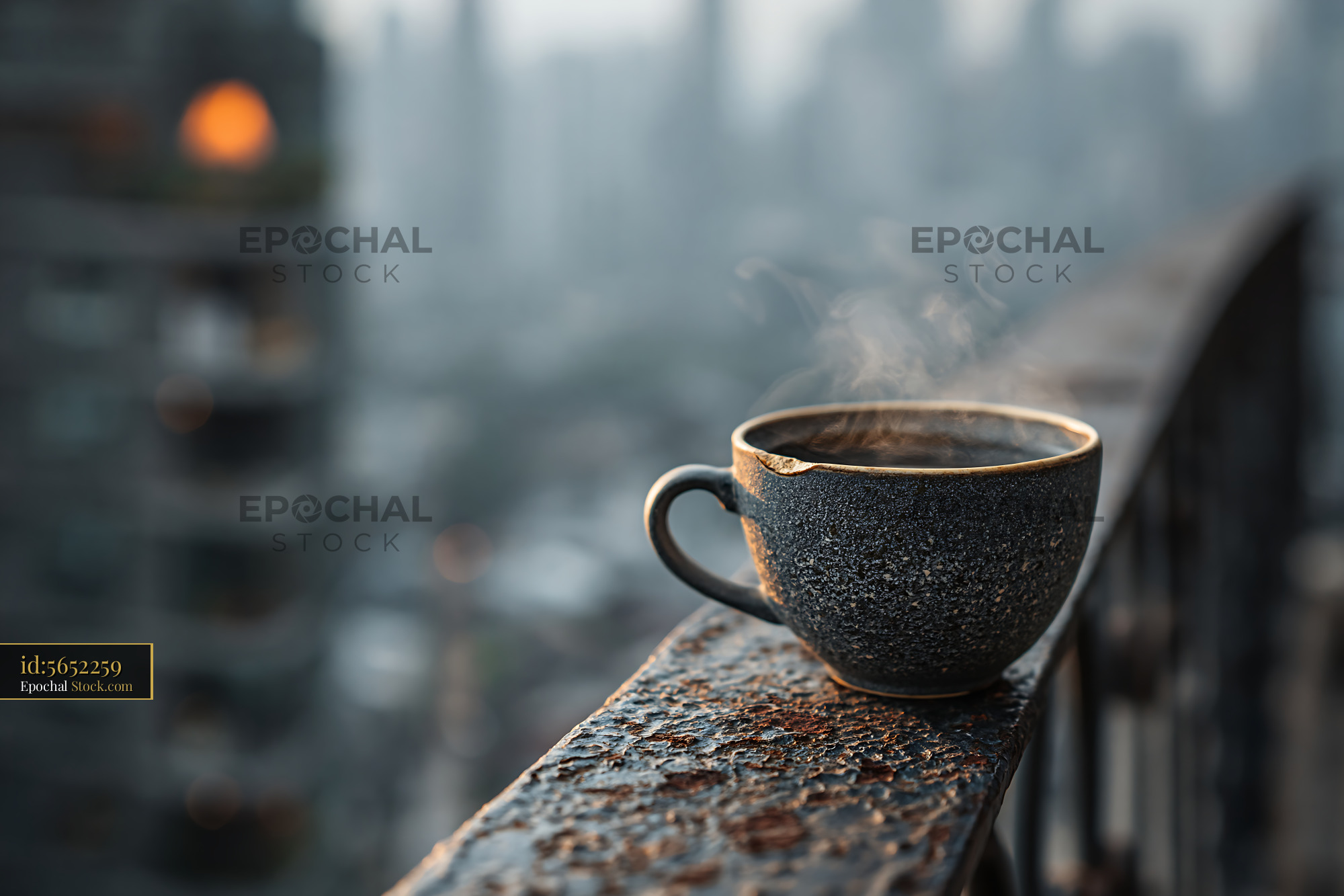 Steaming coffee cup on a rusty balcony railing overlooking a foggy cit - stock photo