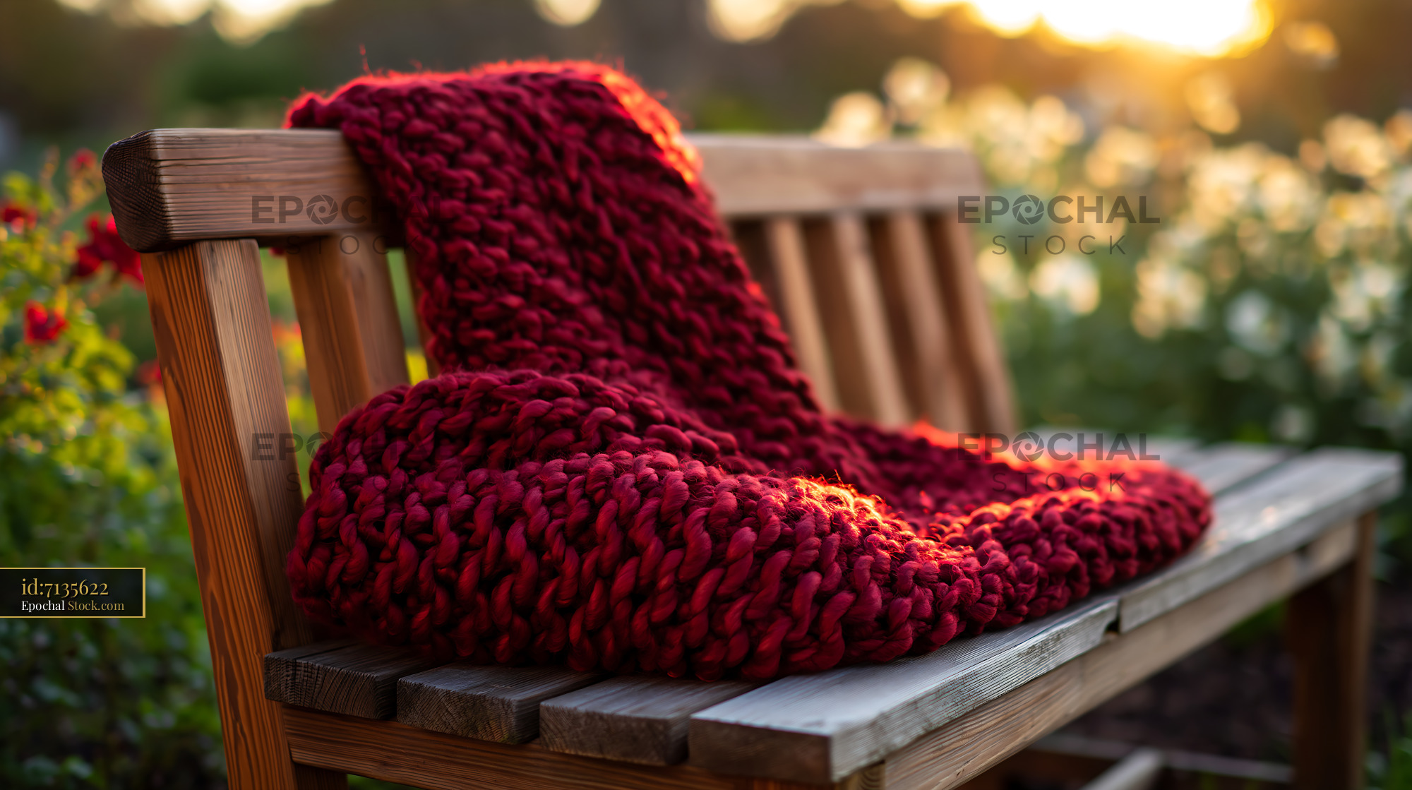 Red chunky knit throw on a wooden garden bench at sunset - stock photo