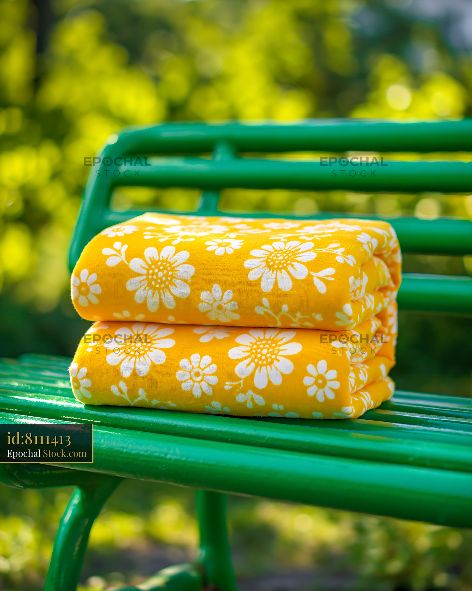 Yellow floral blanket folded on a green metal bench in a sunny park - stock photo