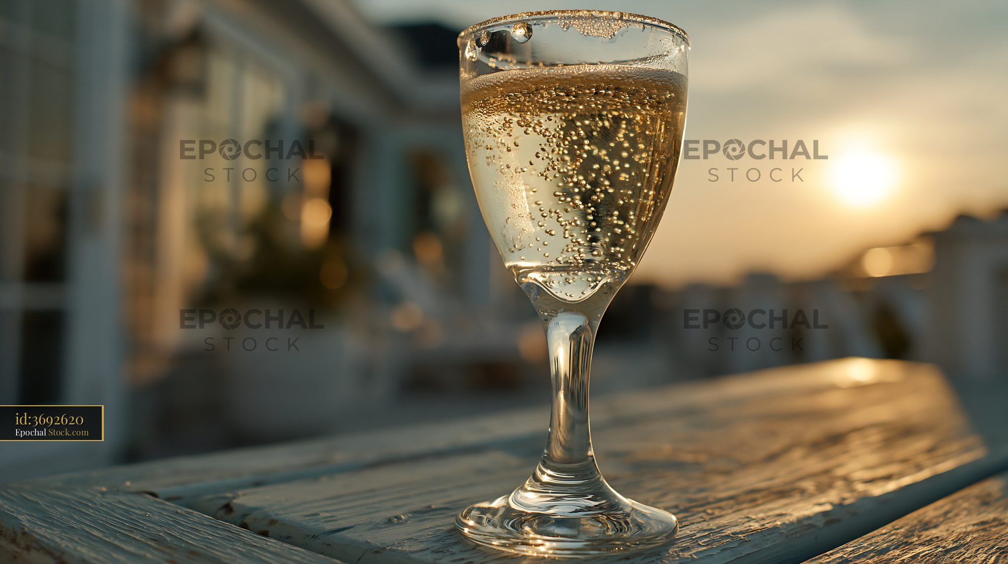 Glass of sparkling wine on wooden table at sunset - stock photo