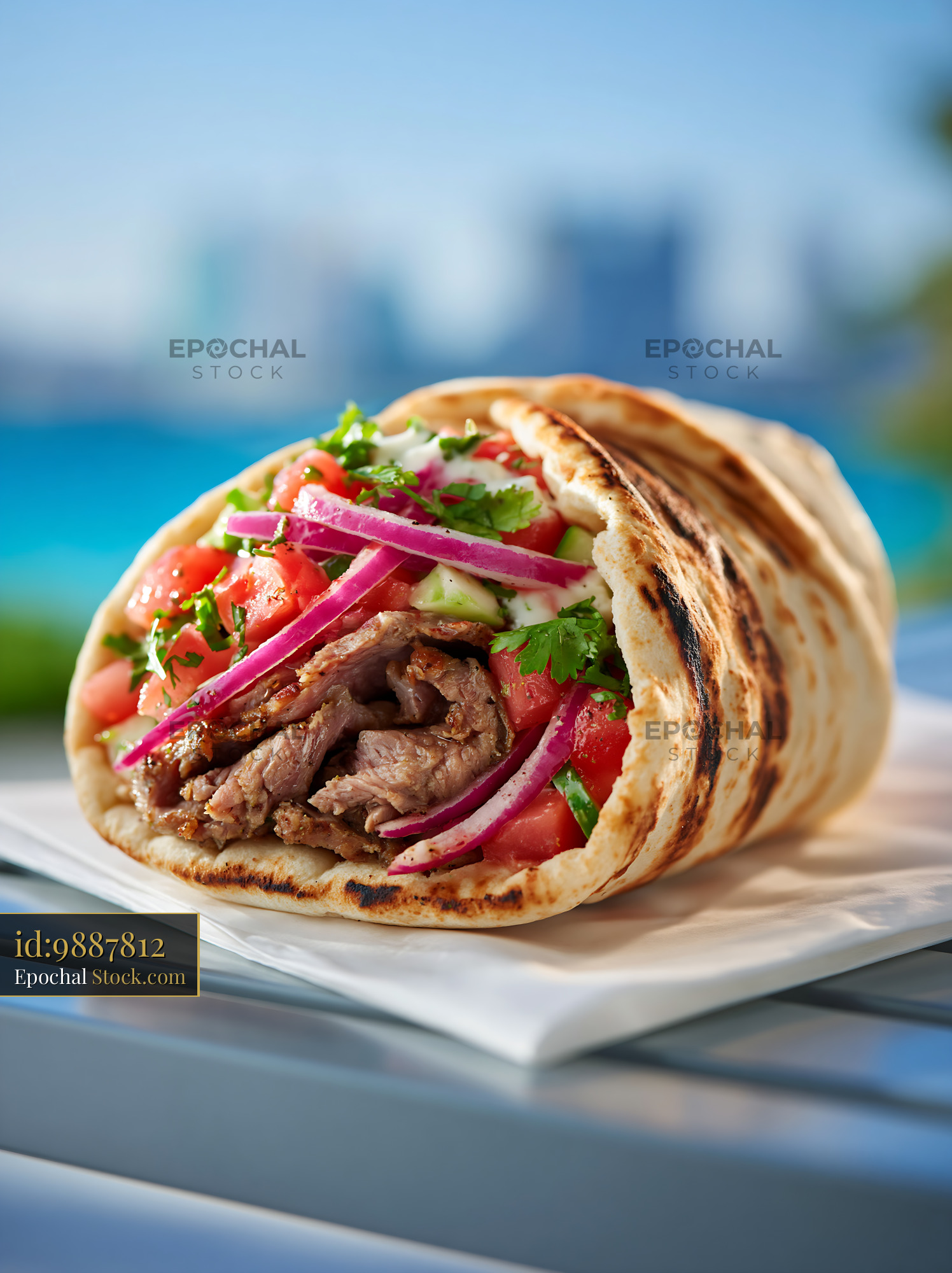 Fresh grilled meat wrap with vegetables on a park bench by the sea - stock photo