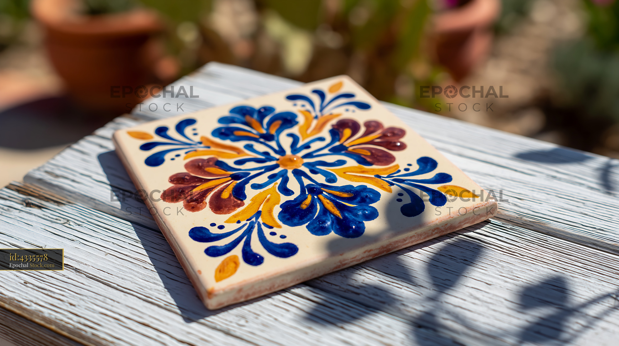 Hand-painted Mediterranean ceramic tile on weathered wood in sunlight - stock photo