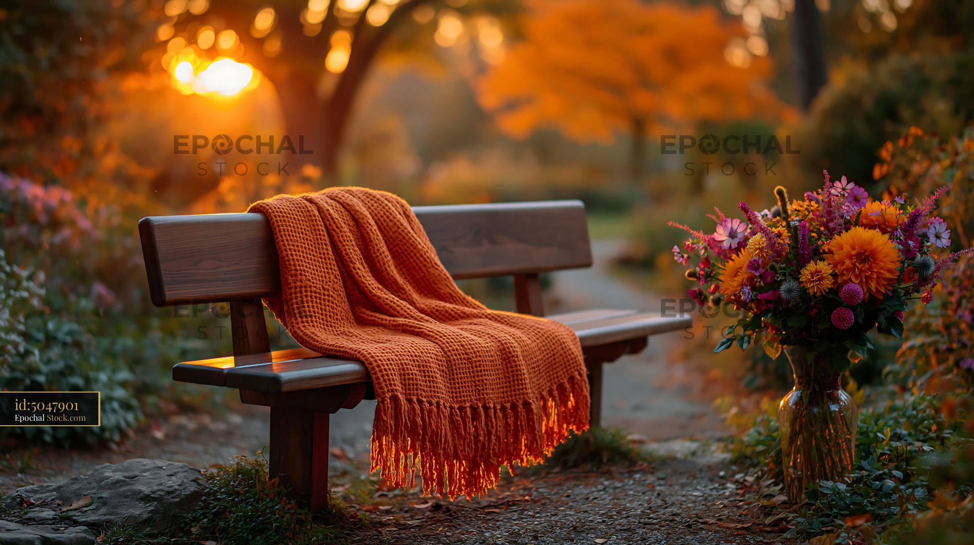 Orange patterned blanket on park seat with autumn flowers at sunset - stock photo