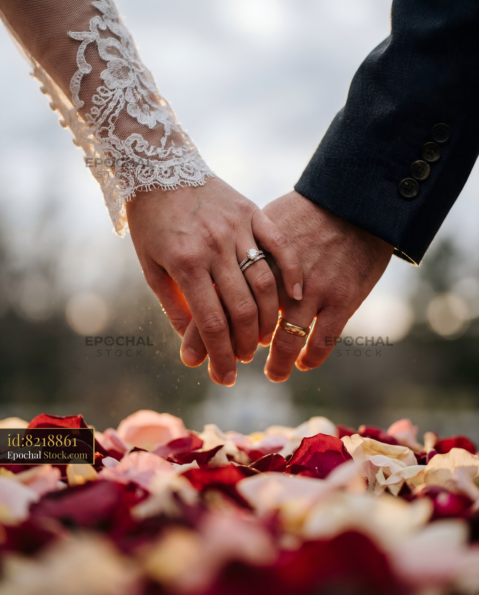Couple holds hands surrounded by rose petals in outdoor space Premium Stock Photo - stock photo
